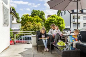 Drei Kinder und ein Erwachsener unter Sonnenschirm auf der Sommerterrasse